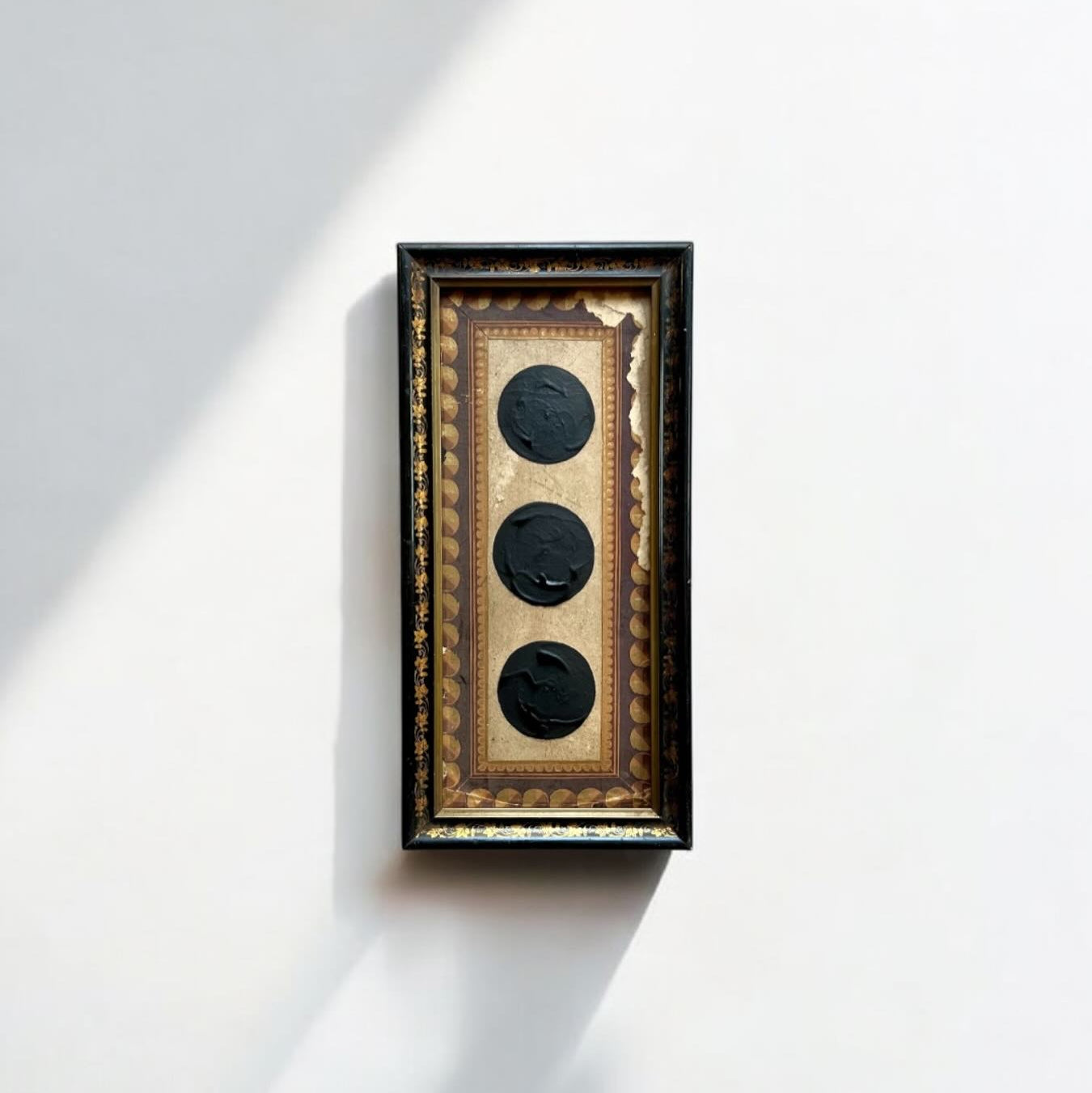 Decorative wall art with three circular black elements in a wooden frame on a white wall.