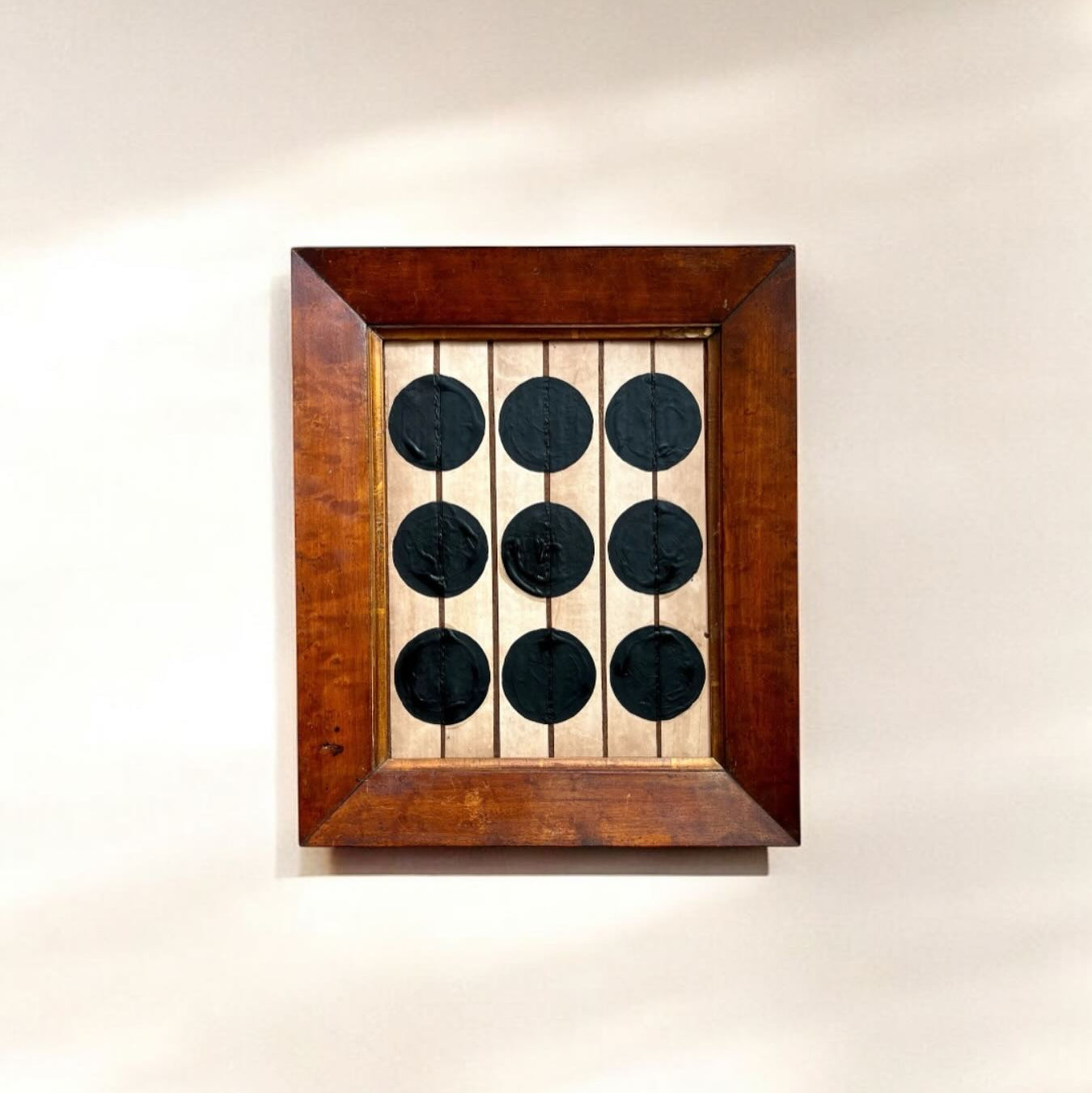 Wooden frame with six black circular objects on a white wall.