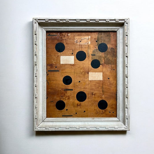 Framed artwork with wooden panel and circular cutouts on a white wall