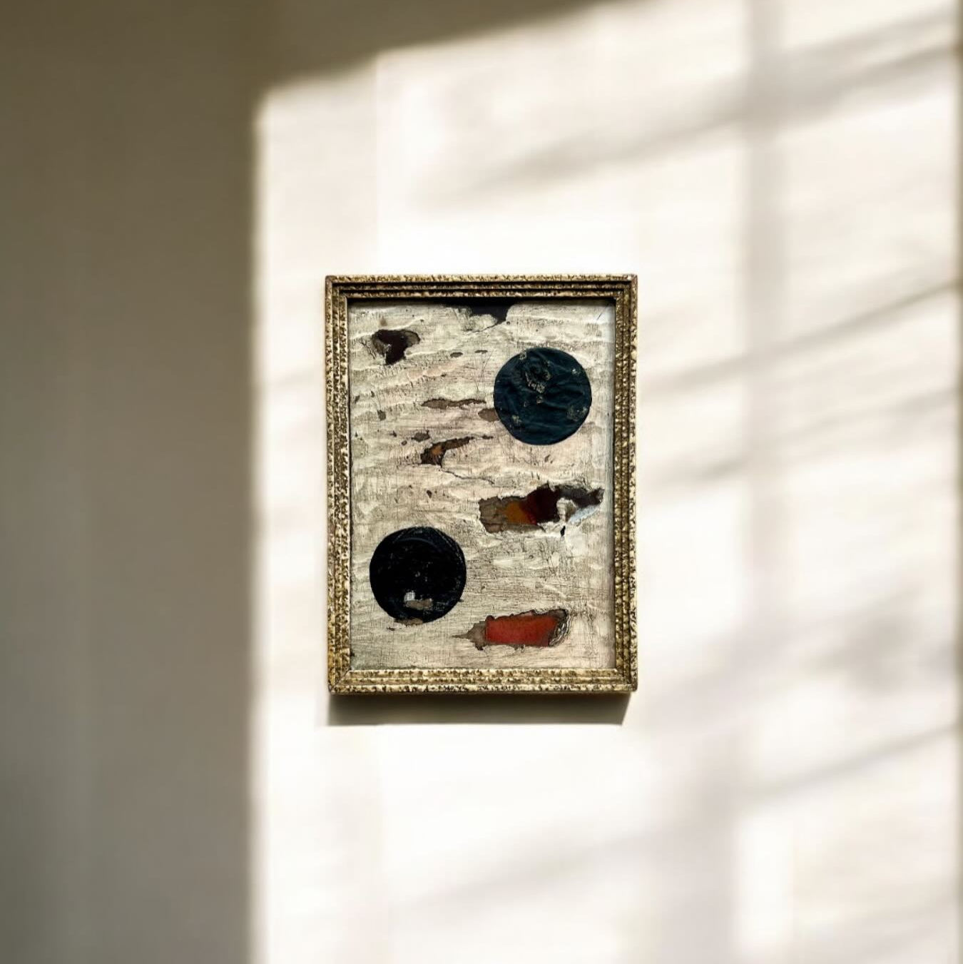 Framed artwork with abstract designs on a wall with light shadows