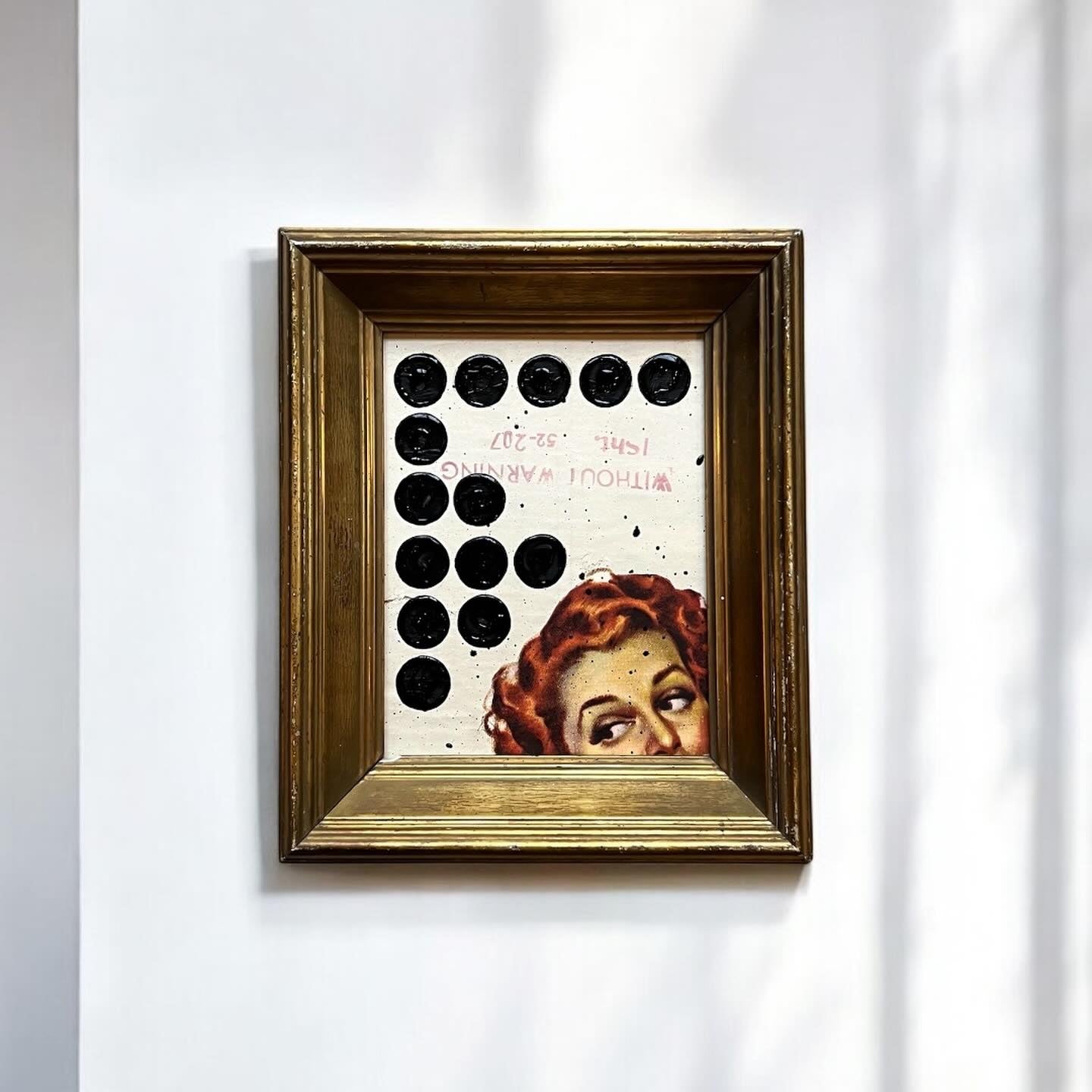 Framed artwork with a stylized face and circular patterns on a white wall.